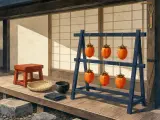 Six bright orange persimmons hang to dry on a wooden rack on a traditional Japanese veranda.