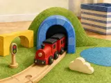 A red wooden toy train emerging from a tunnel in a green toy hill on a play mat.
