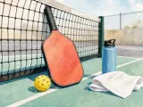 Pickleball paddle, yellow ball, water bottle, and towel resting on an outdoor court beside the net.